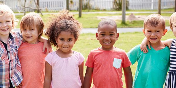 Group of children smiling at the camera while standing outdoors.